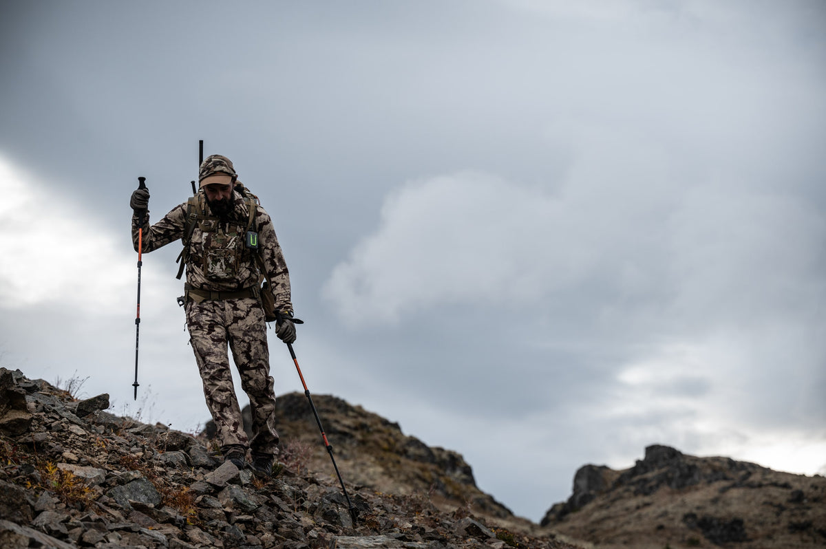 Black trekking pole with orange sections, held by a hiker on rocky terrain.