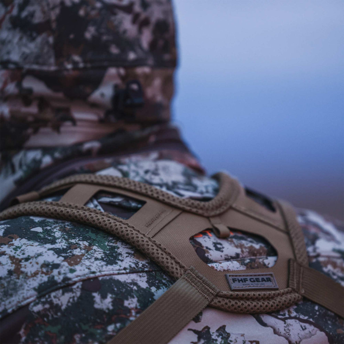 Close-up of a tan FHF Gear binocular harness with mesh straps worn over a camouflage jacket from the back.