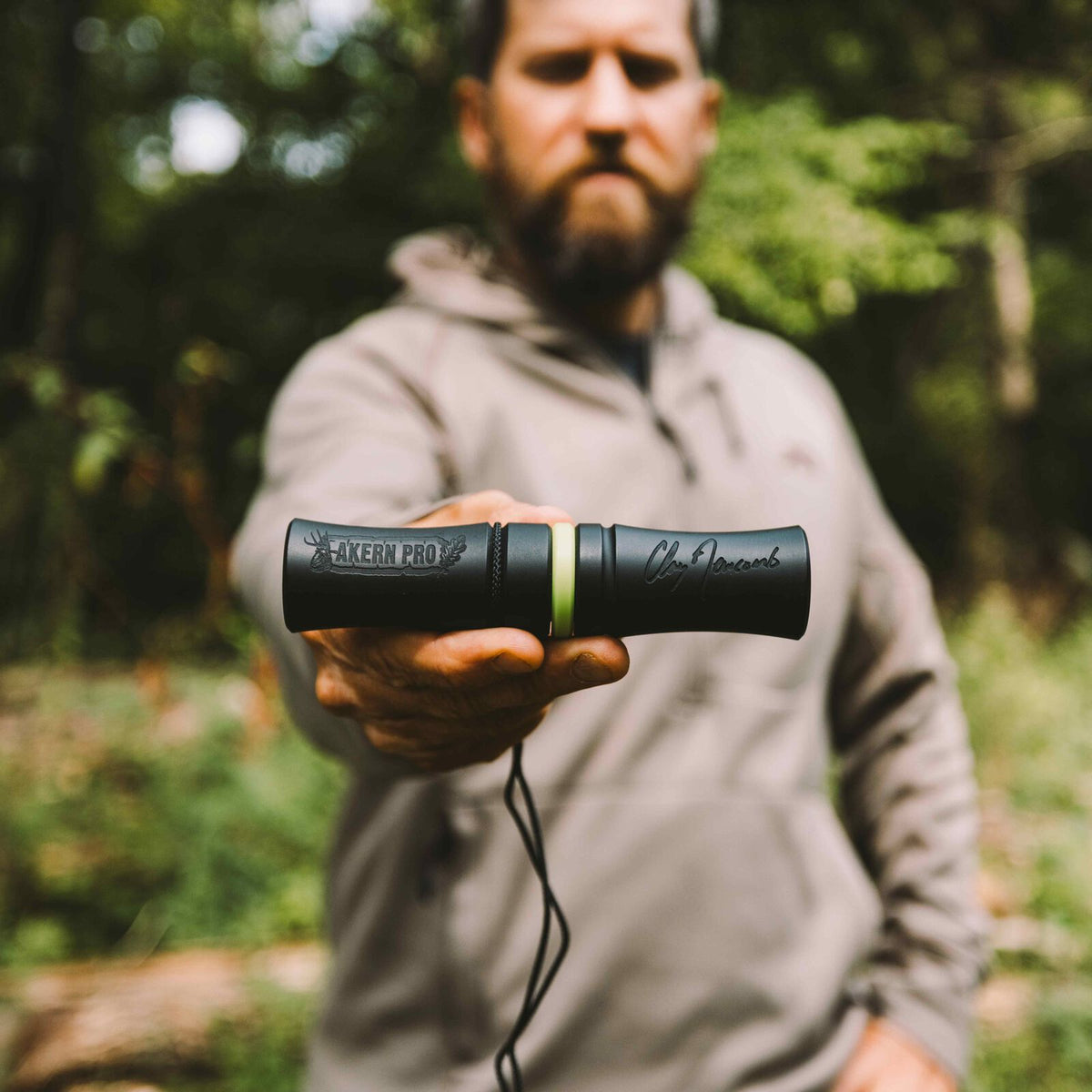 Black Akern Pro hunting call with an antler logo, lime green band, and Clay Newcomb signature, held by a man.