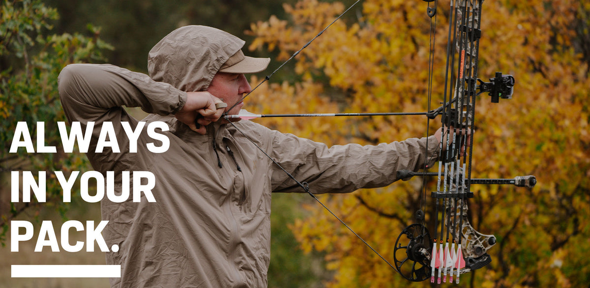 Tan-clad hunter aims camouflage compound bow with nocked arrow.