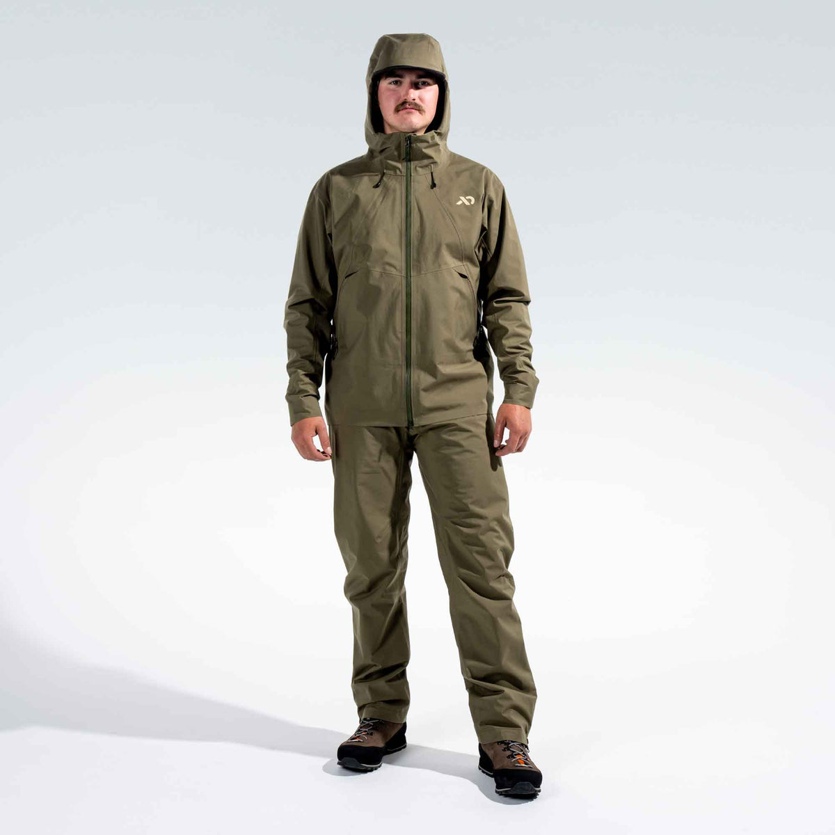 A man wearing a matching olive green waterproof hooded Borah jacket and pants set, standing against a light gray studio background.