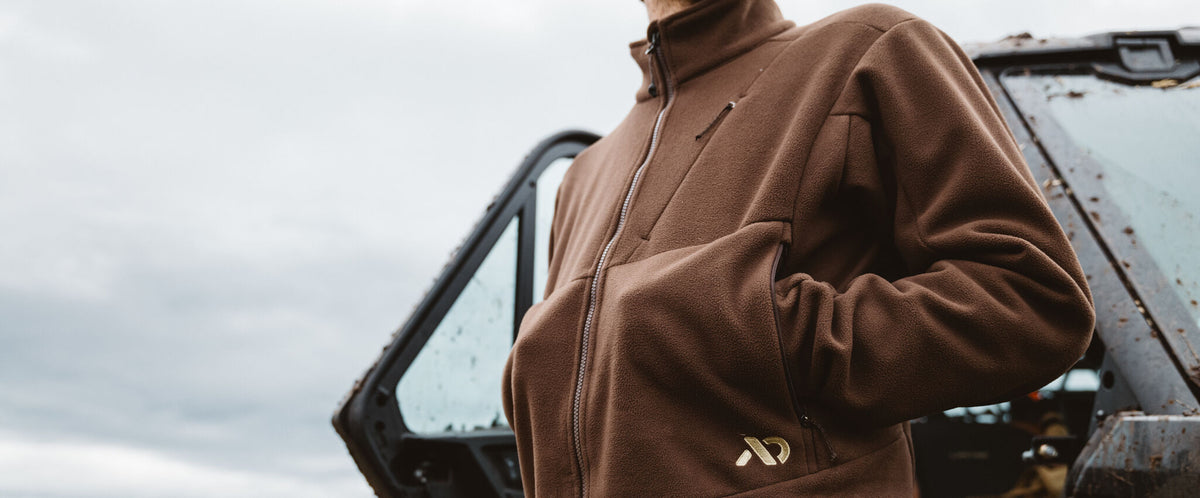 Brown fleece jacket with full zipper, chest pocket, side pockets, and gold logo.