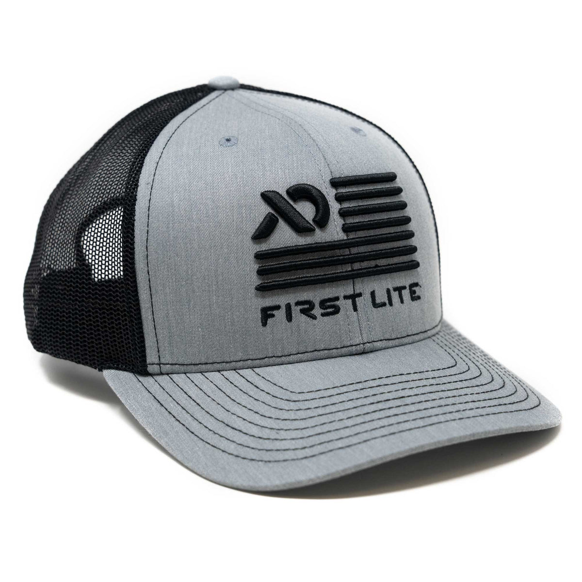 A grey and black trucker hat featuring a raised black "AD" logo, horizontal stripes, and "FIRST LITE" text on the front, with a black mesh back.