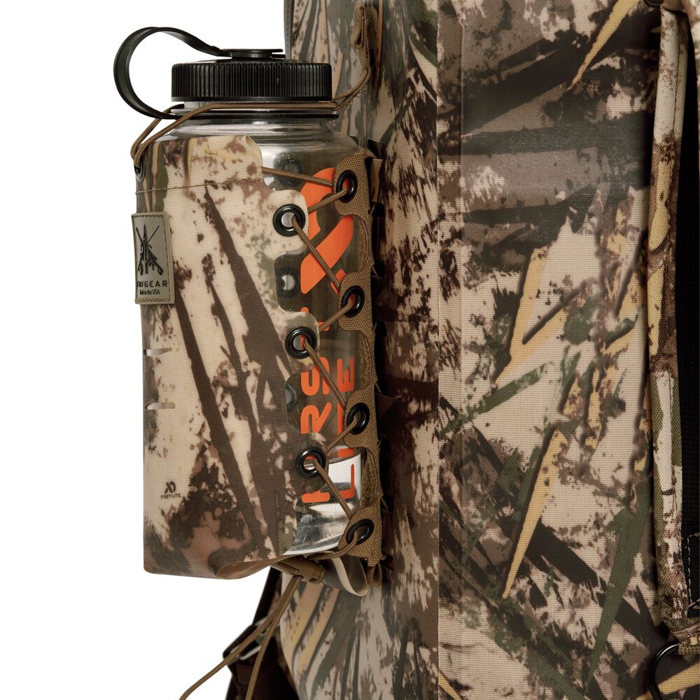 A clear water bottle with a black cap and orange text is held in a camouflage fabric holder with tan lacing, attached to a camouflage backpack.