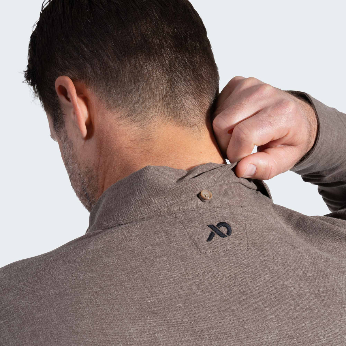 Man adjusting collar of a brown shirt with a logo on a white background