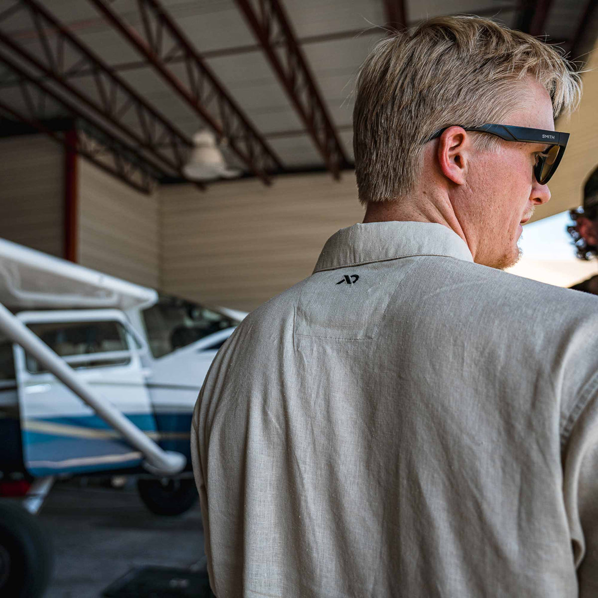 Man wearing sunglasses inside an airplane hangar with a small aircraft visible.