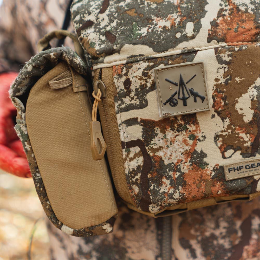 FHF GEAR multi-color camouflage binocular harness with a tan side pouch and a square hunting logo patch.