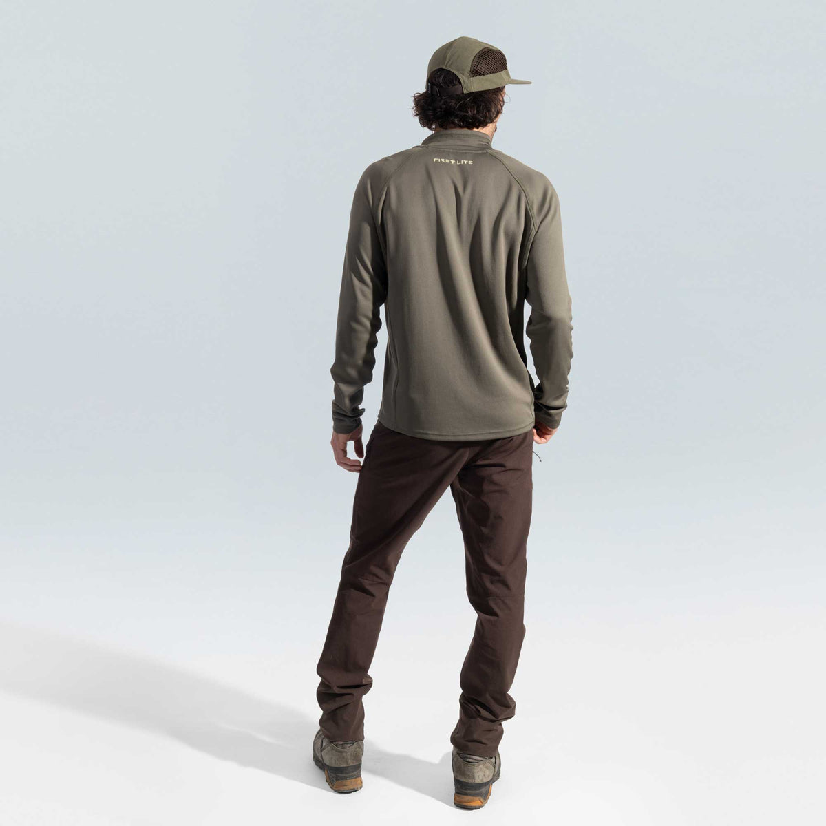 Person wearing a green quarter zip and brown pants on a light gray background