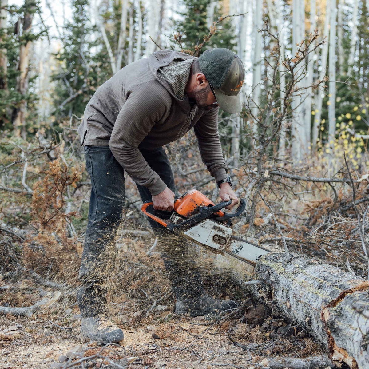 Person using a chainsaw to cut through a log in a forest setting