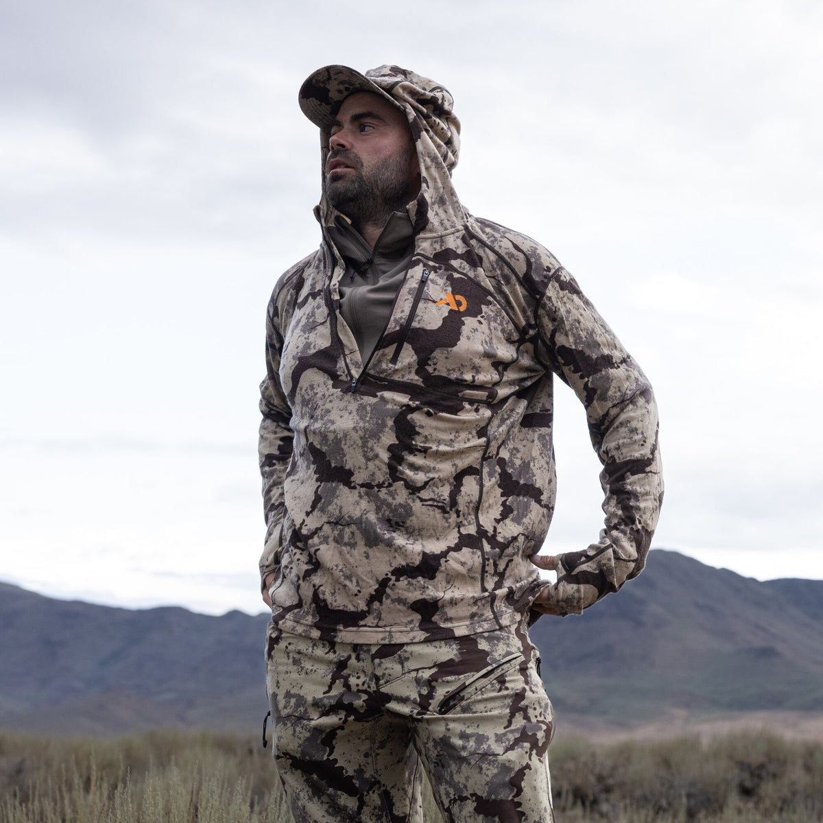 Men's desert camouflage hunting set: quarter-zip hoodie with an orange logo, matching pants, and cap.