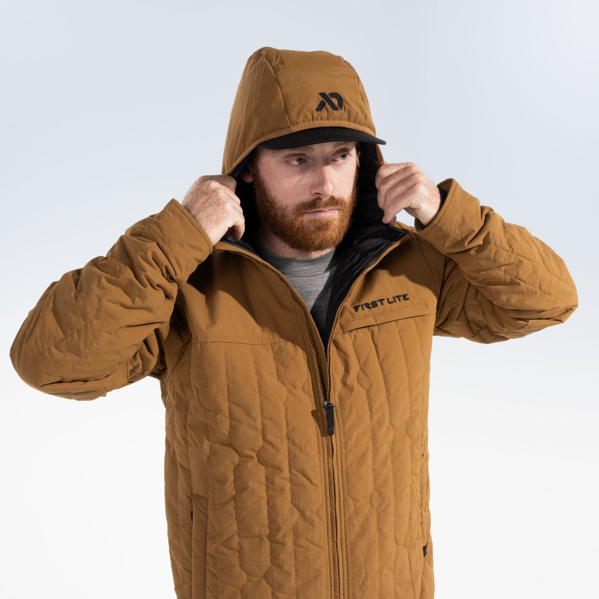 Man wearing a rust outpost jacket that has black FIRST LITE branding on the left chest and black FIRST LITE logo on the jacket hood.