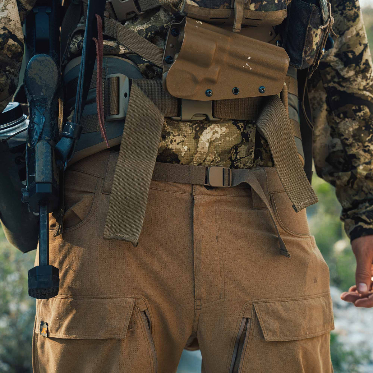 Brown tactical pants with cargo pockets and a textured fabric, worn with a coyote brown tactical belt, holster, and a rifle.