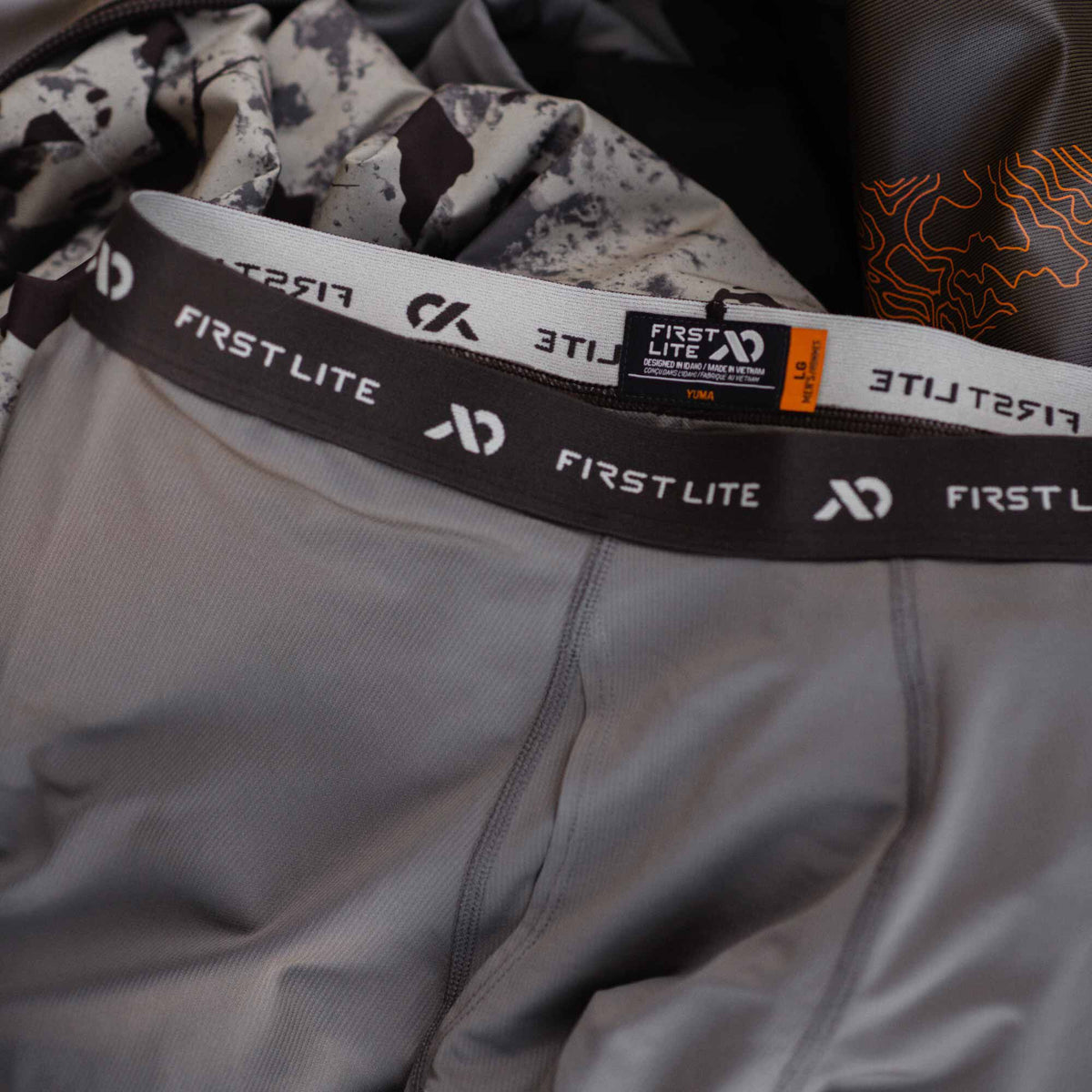 Grey men's First Lite Yuma base layer bottoms with a dark brown elastic waistband featuring the brand name.