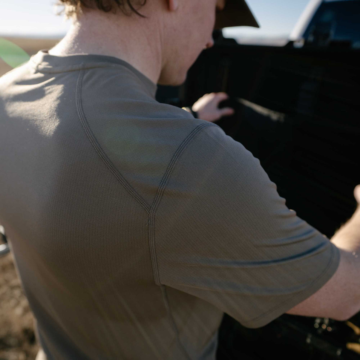Olive green short-sleeved textured knit shirt with flatlock seams across the shoulders and back.