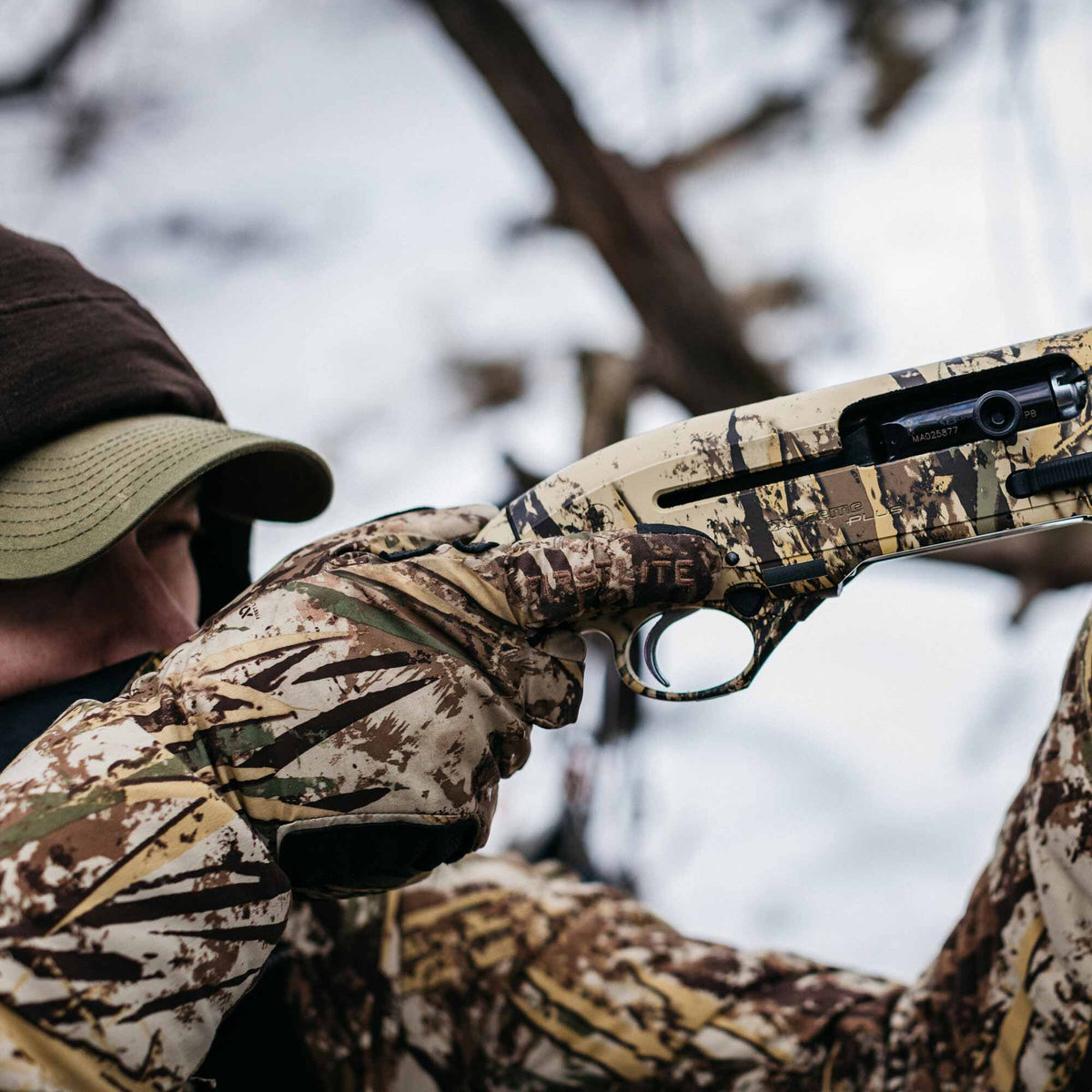 Close-up of a Beretta A400 Xtreme Plus semi-automatic shotgun in a tan and brown camouflage pattern, held by a person wearing matching First Lite camo gloves.