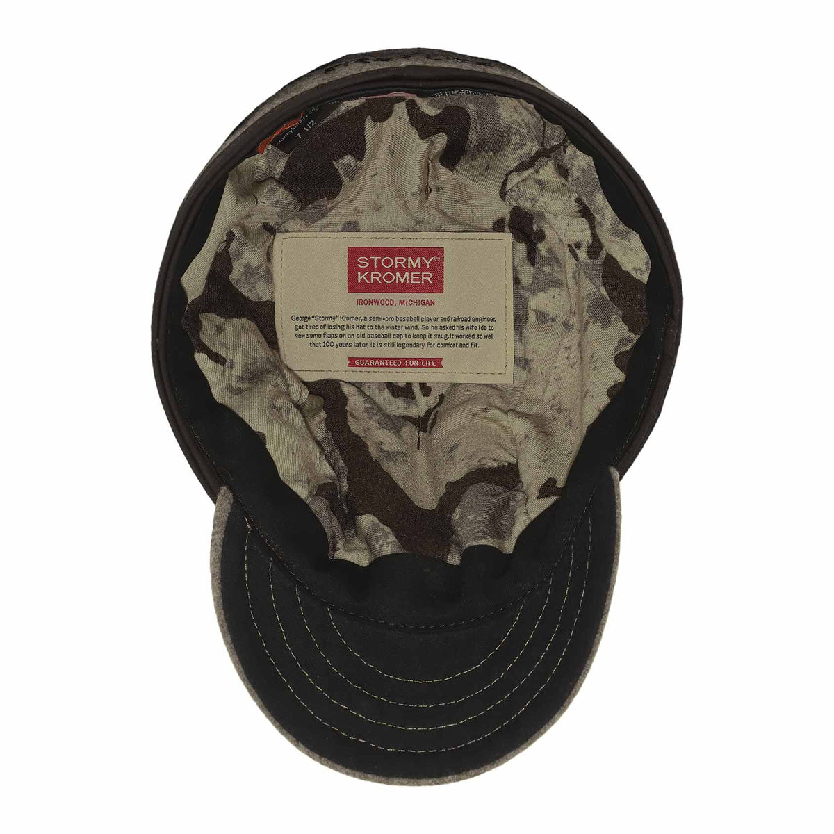 Upside-down Stormy Kromer cap with a gray brim, dark brown exterior, and a green/brown camouflage interior lining with a visible brand label.