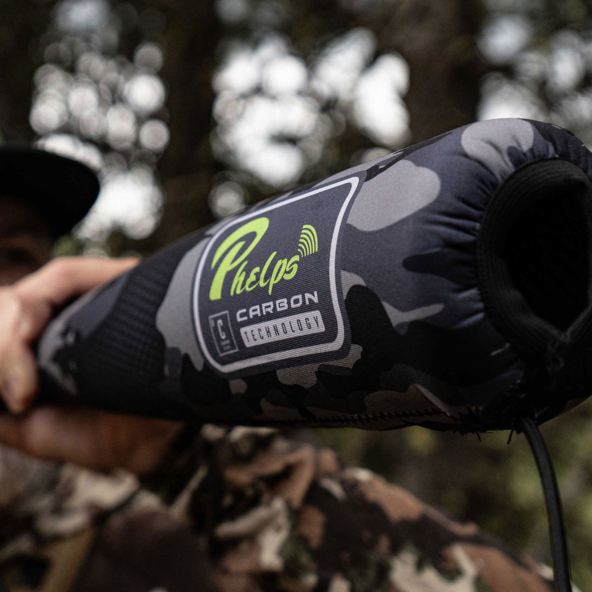 A grey and black camouflage Phelps Carbon Technology game call with a neon green logo and an open black end.