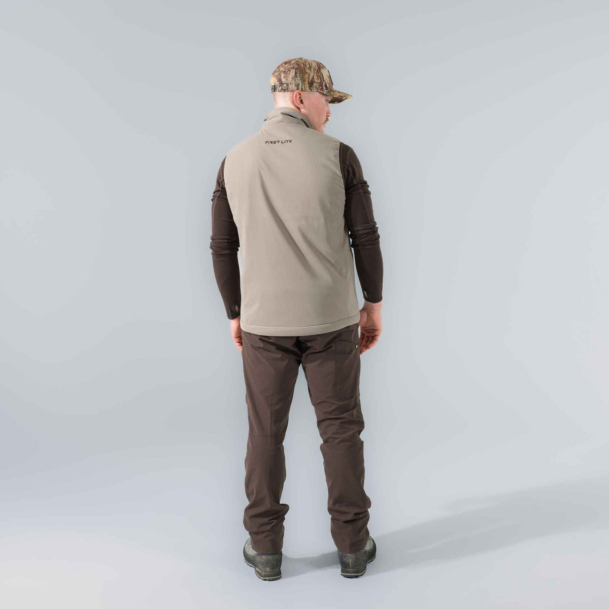 Tan outdoor vest with "FIRST LITE" logo on the back, worn by a man over a brown long-sleeve shirt.