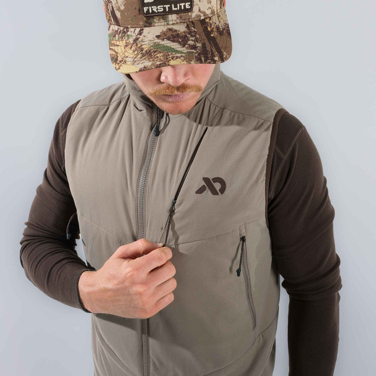 Walnut full-zip vest with a zippered chest pocket and dark logo, being unzipped.