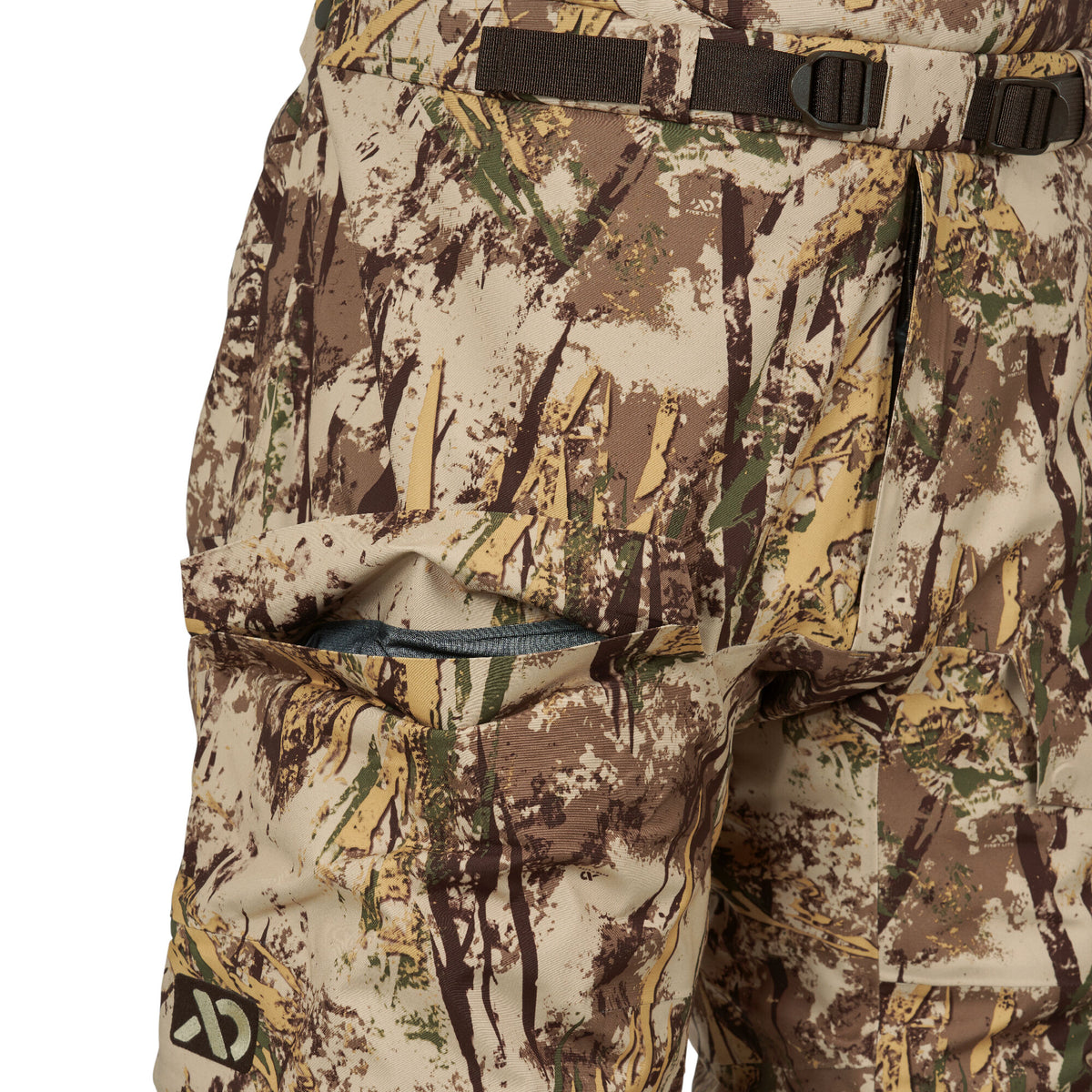 Tan, brown, and green camouflage pants featuring a dark webbed belt with buckles, a partially open side cargo pocket revealing a blue lining, and a First Lite logo.