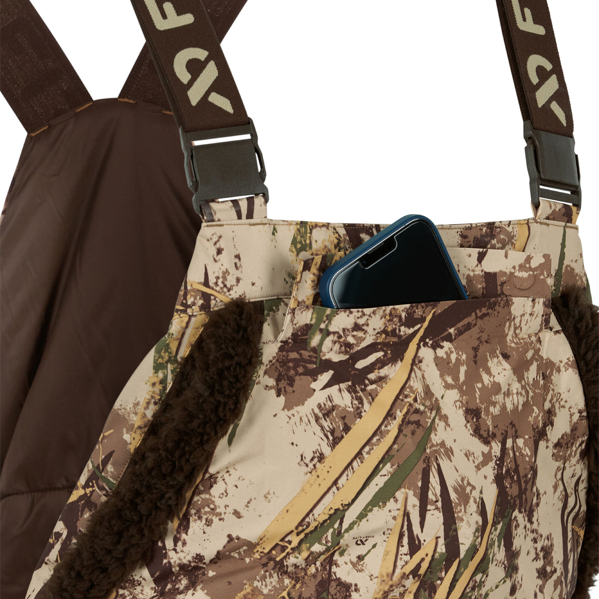 Camouflage bibs with brown fuzzy trim, dark brown straps, and a smartphone visible in a chest pocket.