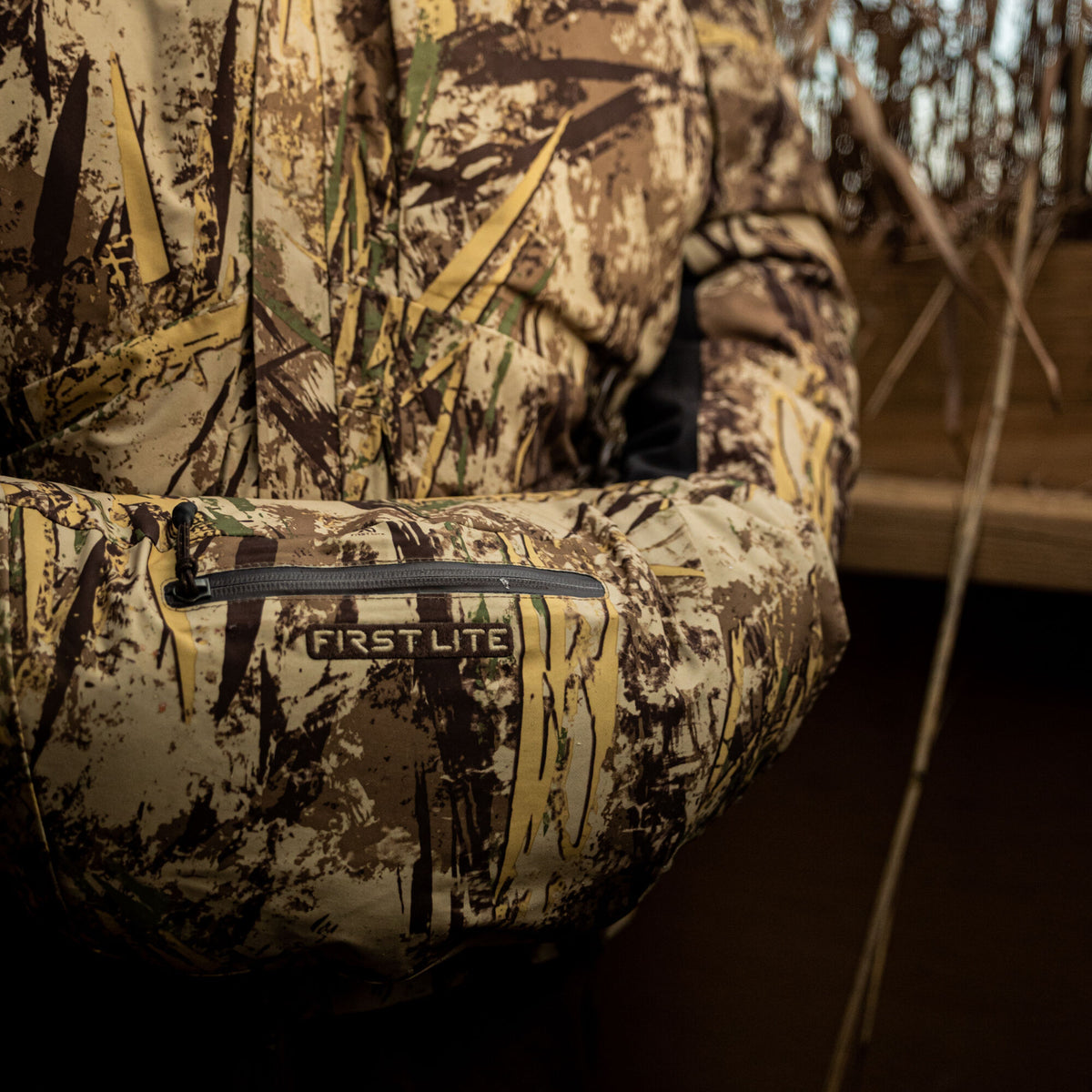 Camouflage jacket sleeve featuring a zippered pocket with a "FIRST LITE" logo.