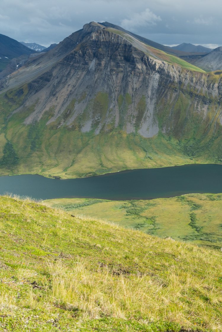 Mountain landscape with a lake and grassy slopes under a cloudy sky.