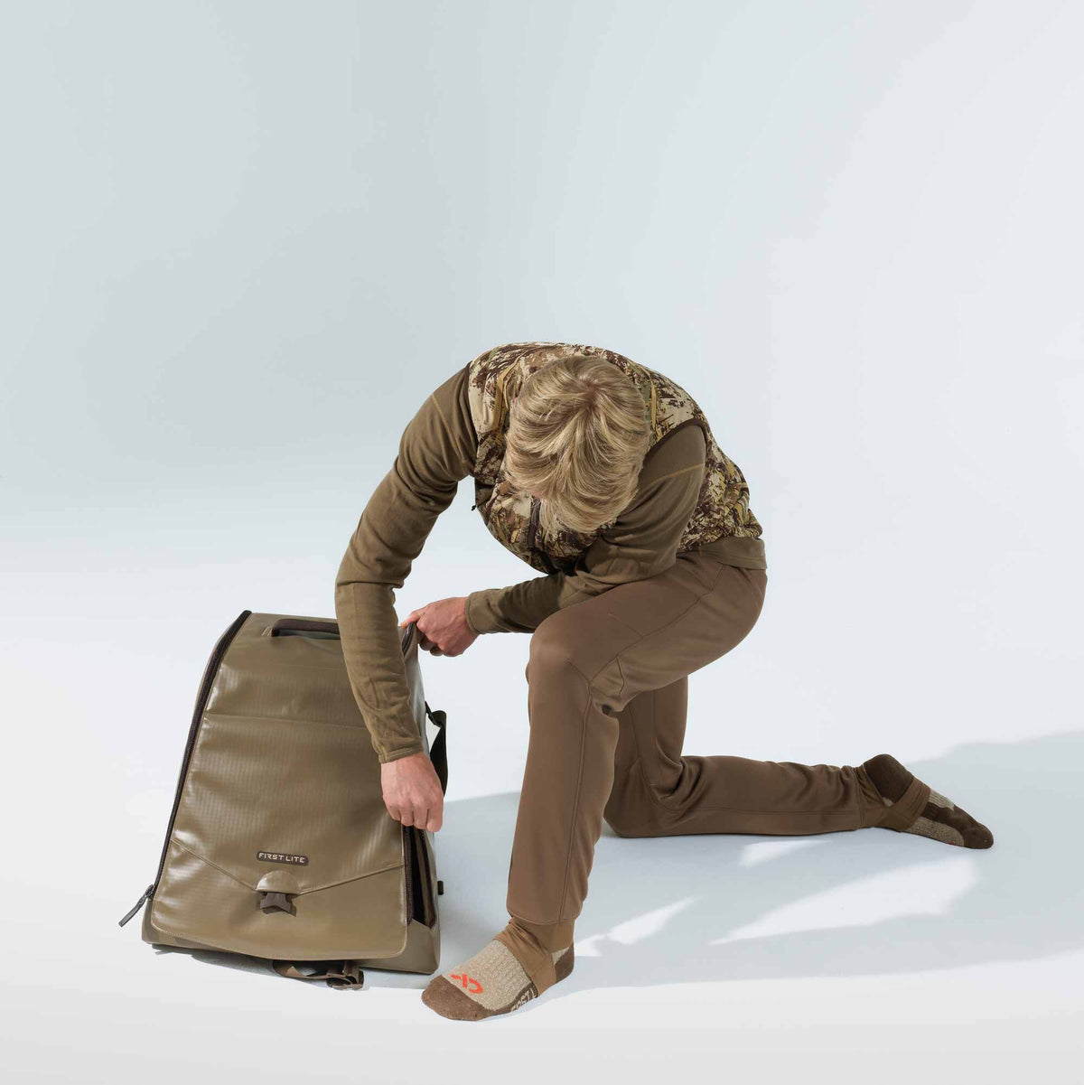 Walnut duffel bag with a zippered main compartment and a buckled front flap featuring the FIRST LITE logo.