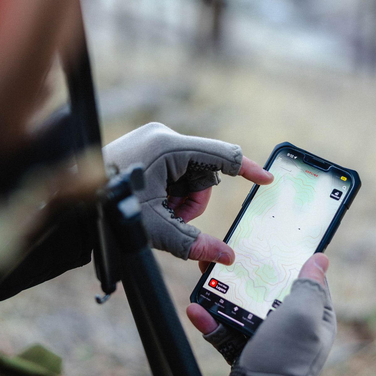 A person wearing grey fingerless gloves uses a black smartphone displaying an offline topographic map.