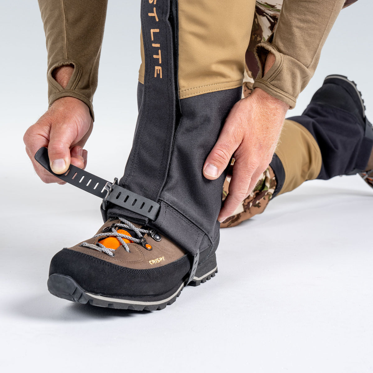 Model wearing First Lite boot gaiters, bending down to adjust boot strap