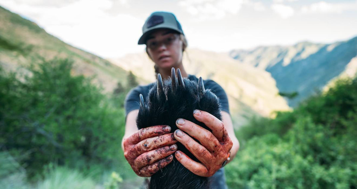 Black bear paw with long, sharp claws, held by bloody hands.