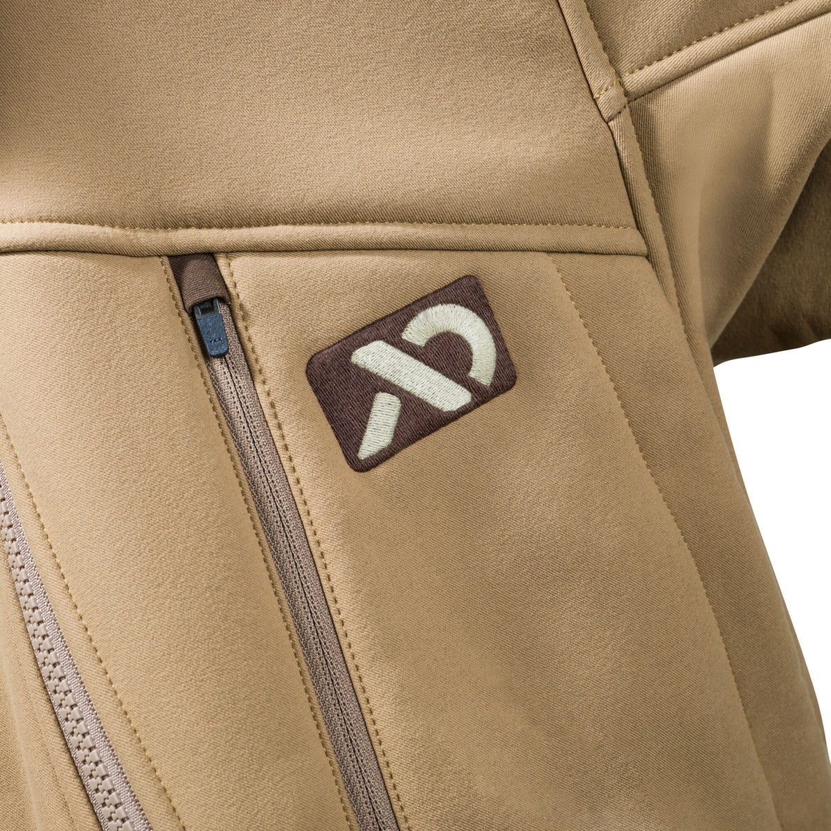 Close-up of a tan jacket showing a vertical zippered pocket and an embroidered brown logo patch with a white abstract symbol.
