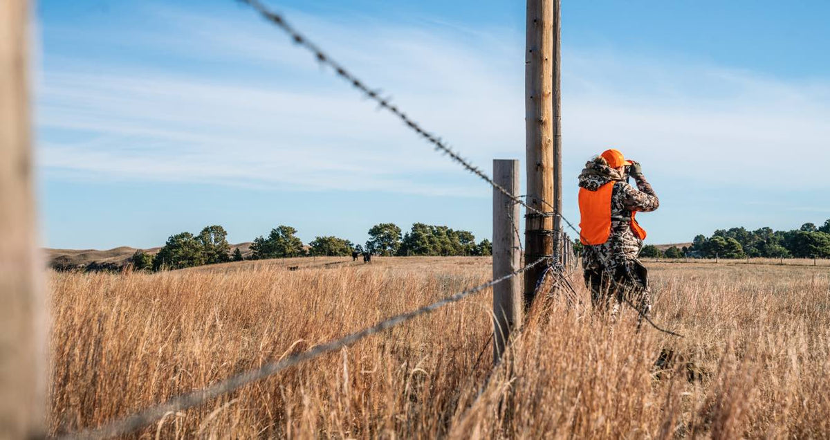 Orange hunting vest and hat over camouflage outfit, worn by hunter with binoculars.