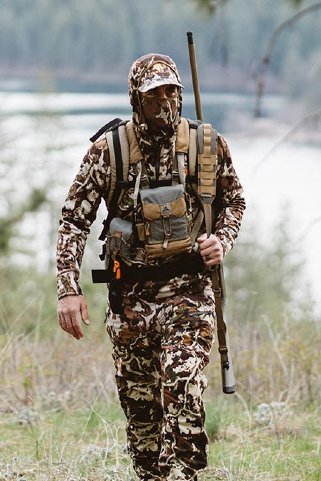 Brown and white camo hunting gear with cap, chest rig, and rifle.