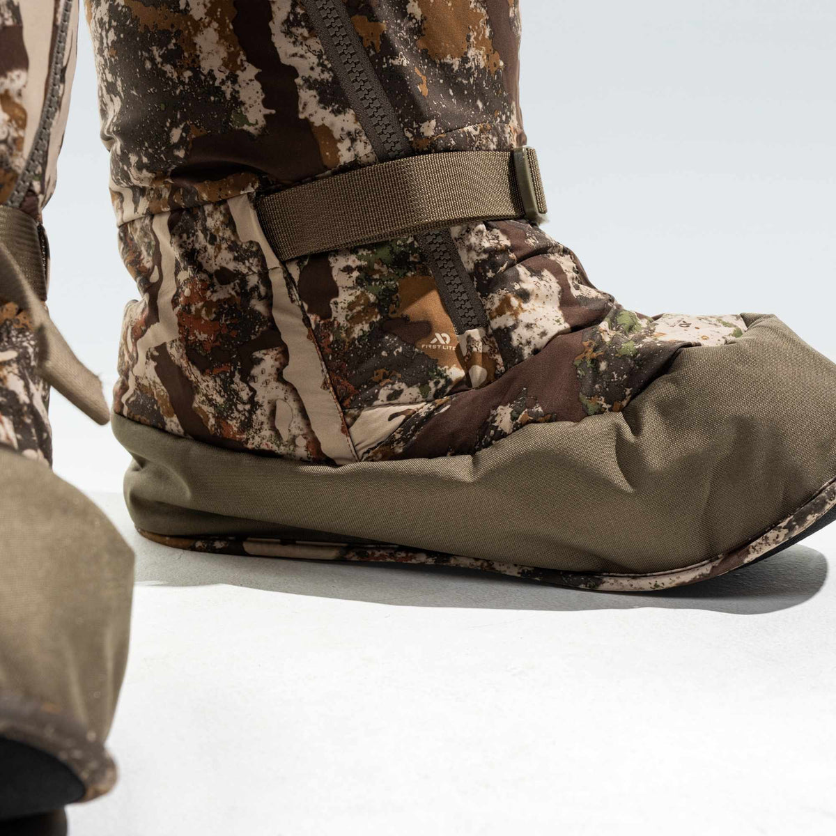 Close up to the base of a camo overboot. It has olive green mesh in its base.
