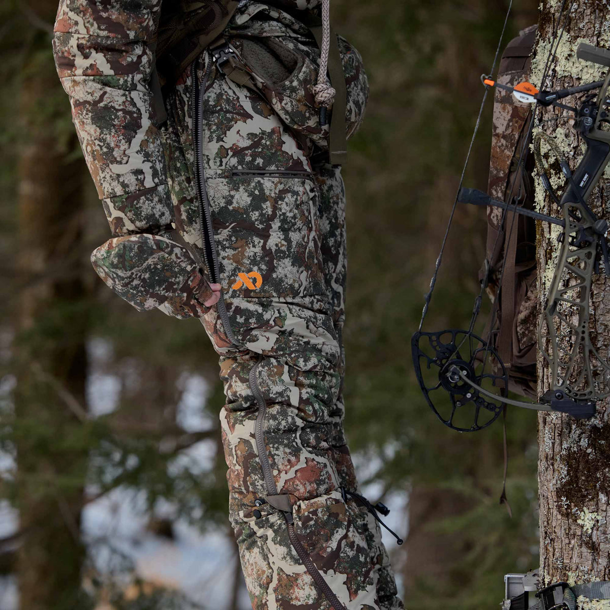 Man in a forest zipping up his FIRST LITE camo pant.