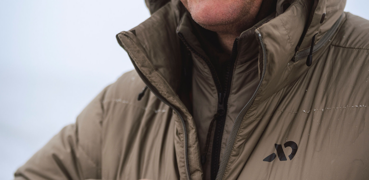 Tan insulated jacket with zipped high collar and black logo on chest.