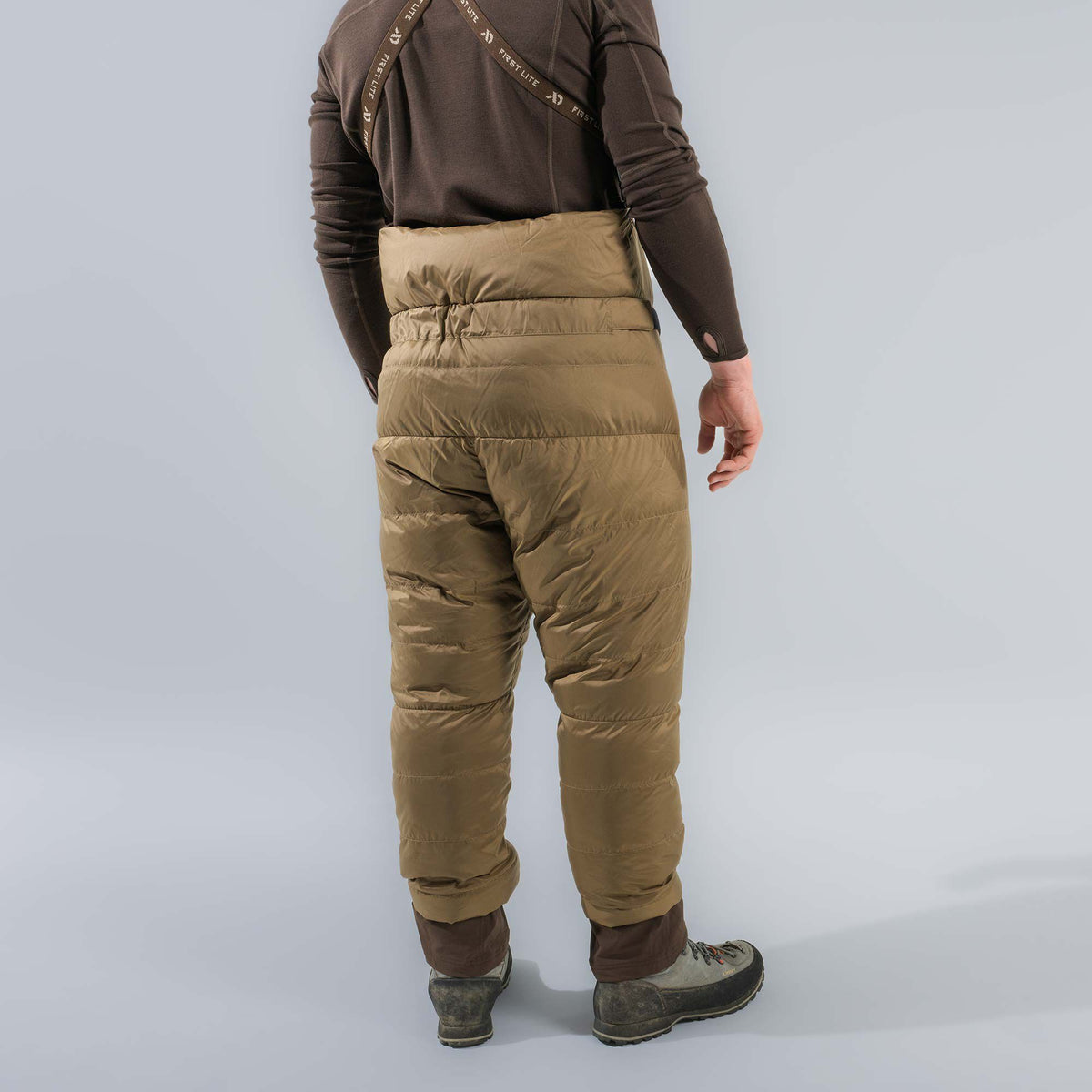 Brown puffy insulated pants with 'FIRST LITE' branded suspenders, worn by a person from behind.