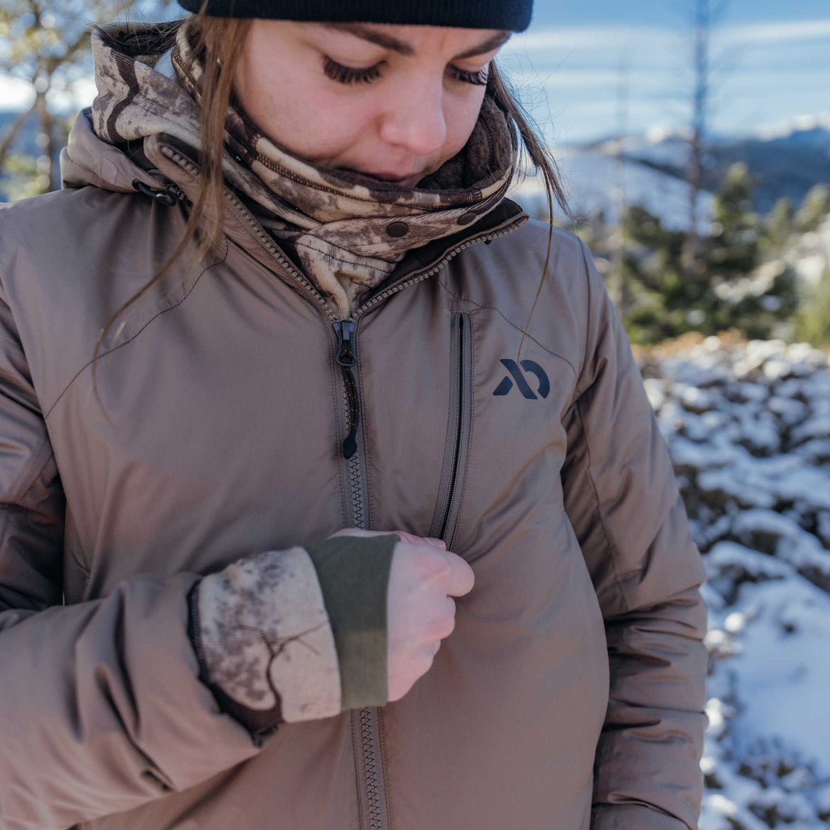 Tan insulated jacket with a full zip front, zippered chest pocket, dark logo on the right chest, and olive green thumbhole cuffs.