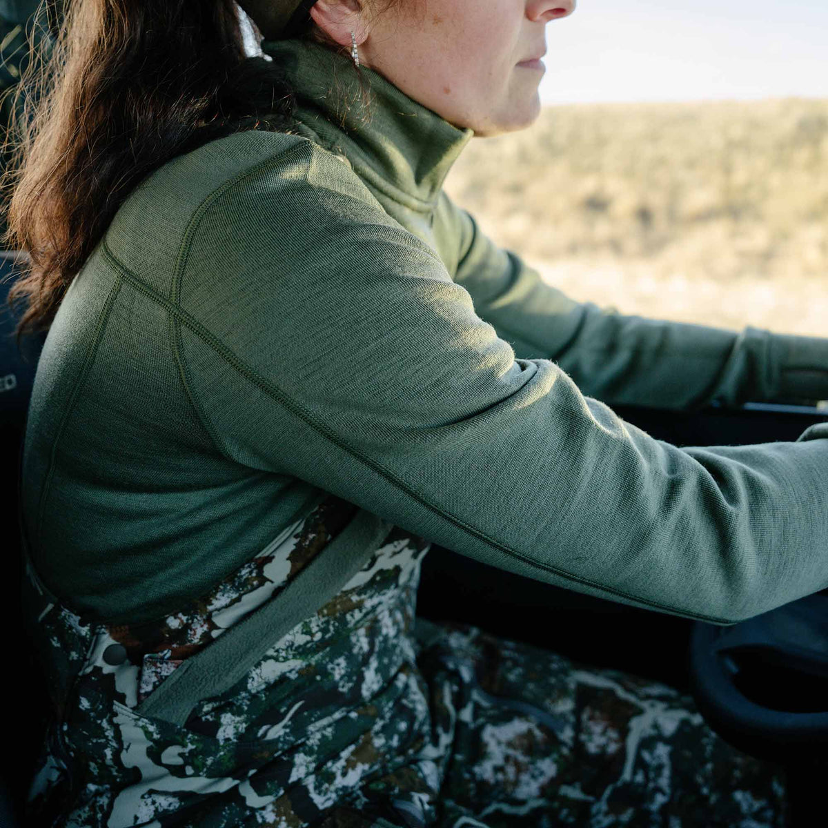Olive green long-sleeve knit shirt featuring a high neck and visible raglan seams, worn by a woman.