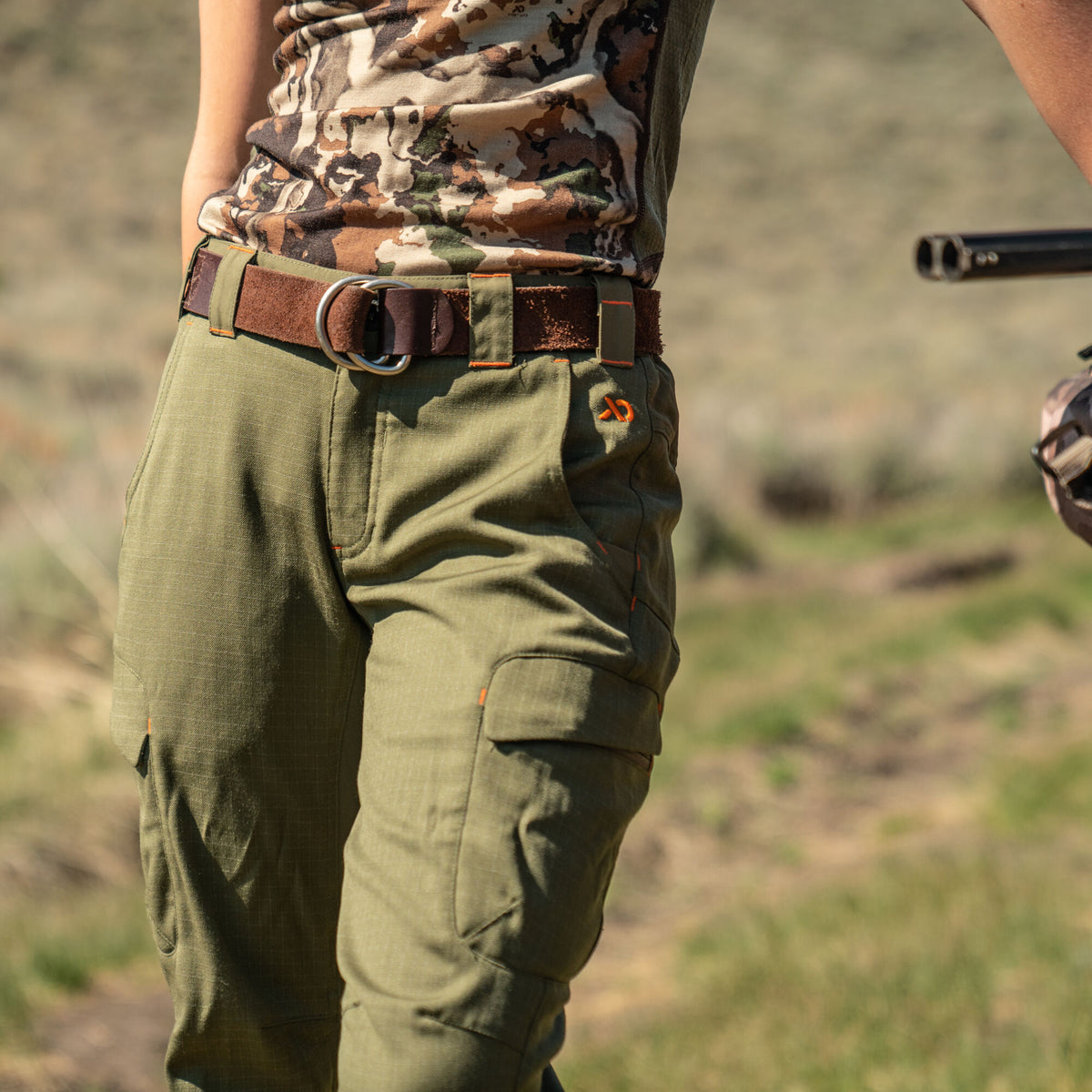 Olive green ripstop cargo pants with orange stitching and logo, paired with a brown D-ring belt.