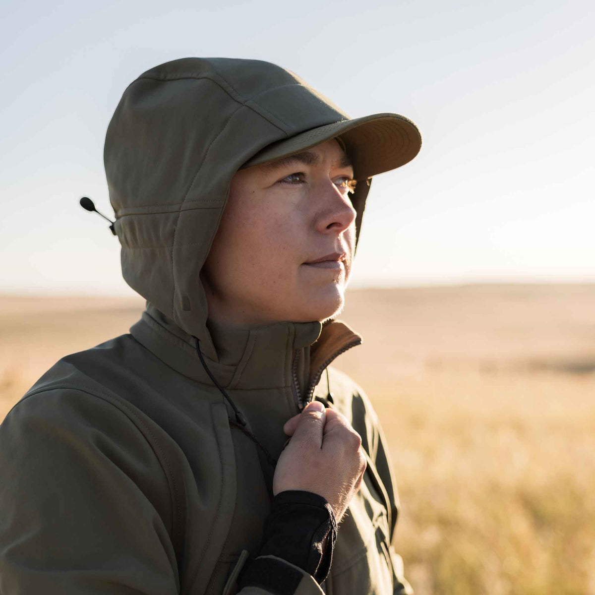 Olive green hooded jacket with a cap brim and drawstring, being zipped up.