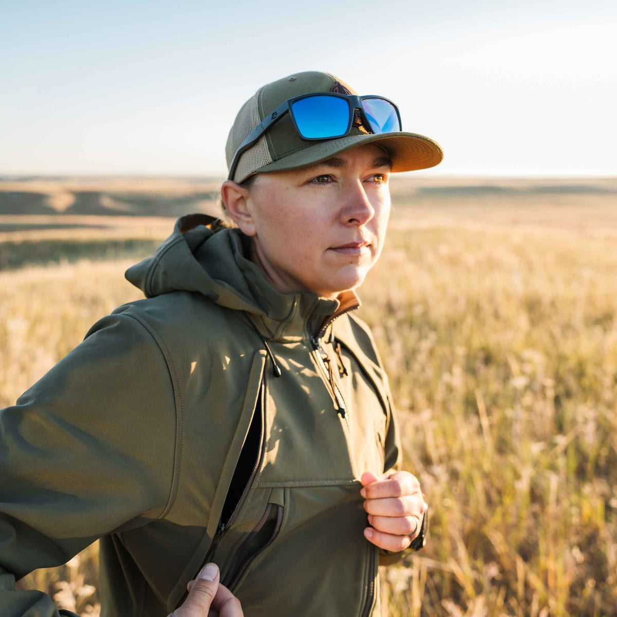 Olive green technical hooded jacket with zippered pockets, one being opened on the side.