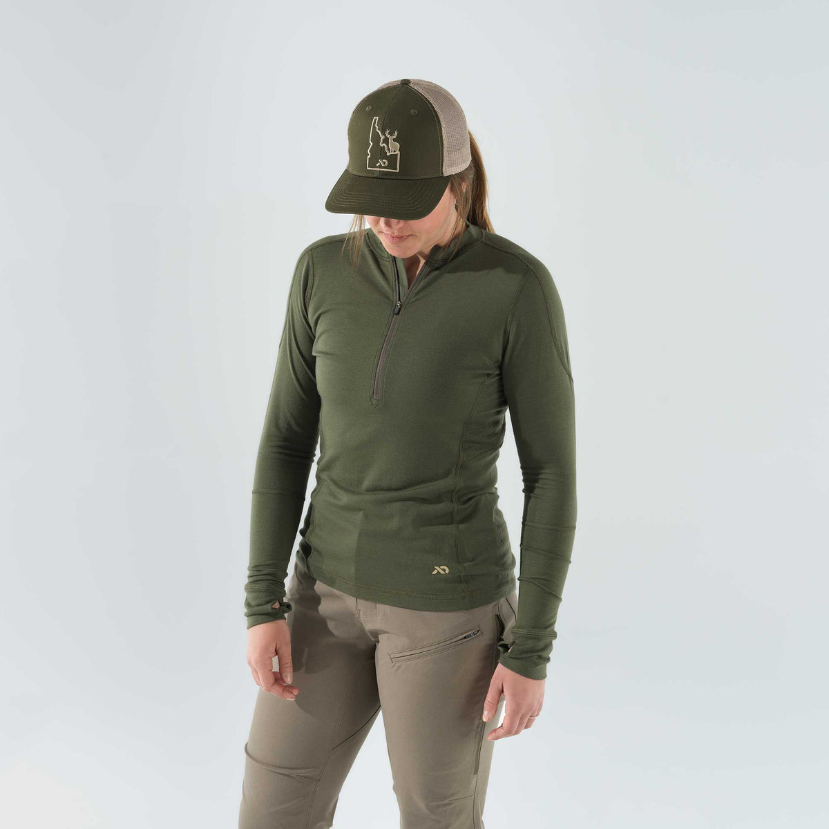 Olive green quarter-zip long-sleeve shirt with thumbholes, khaki pants with zippered thigh pockets, and a green and tan mesh-back hat featuring an Idaho deer emblem.