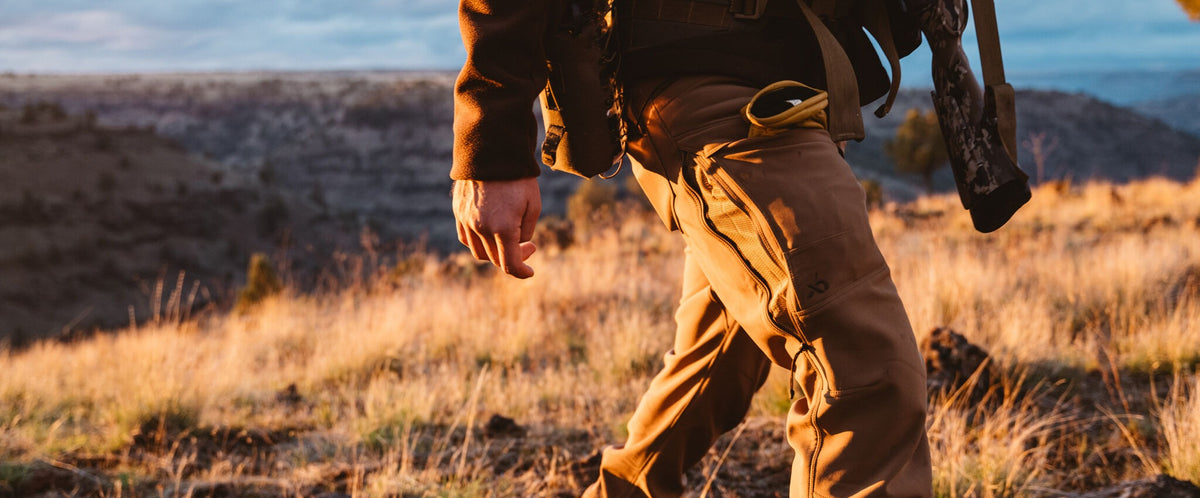 Tan outdoor pants with mesh side panels, cargo pocket, and brand logo.