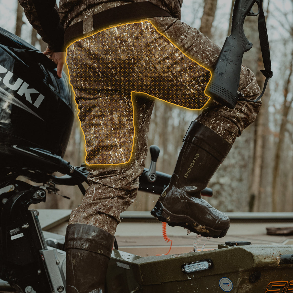 Wet camouflage waders with integrated boots worn by a person stepping into a boat.