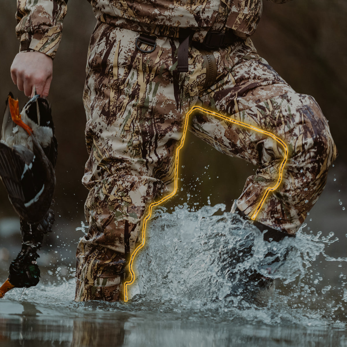 Camo hunting waders with boots splashing in water, holding a duck.