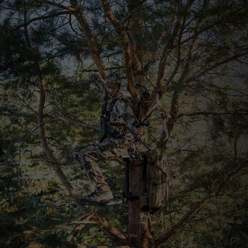 Camo-clad hunter on a dark metal climbing tree stand, with a bow and gear bag.