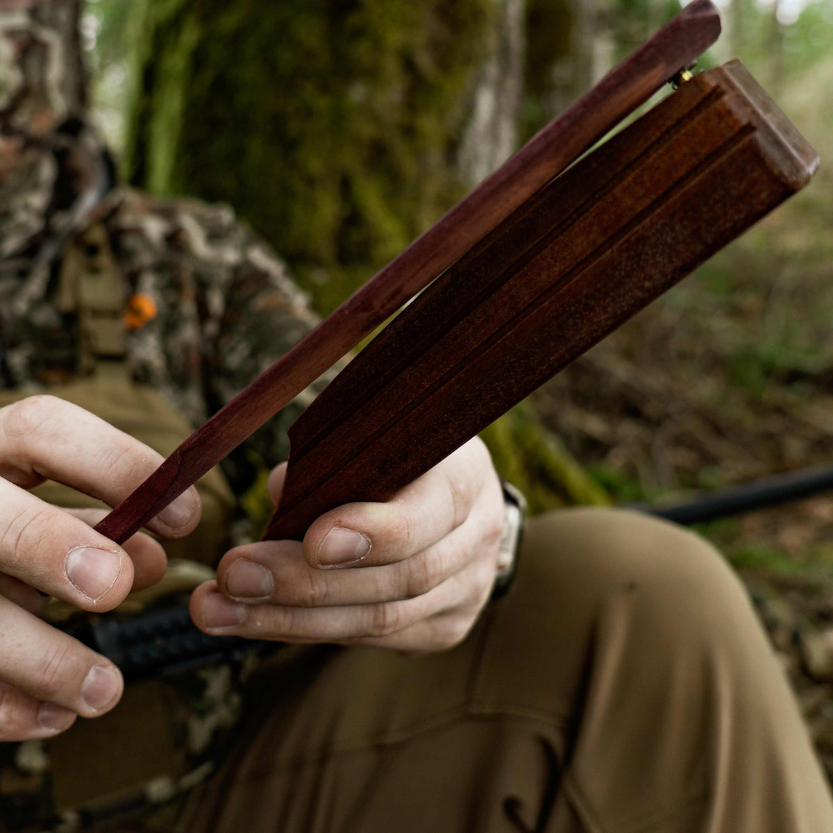 Dark reddish-brown wooden box call with a hinged paddle and brass pivot, held in hands.