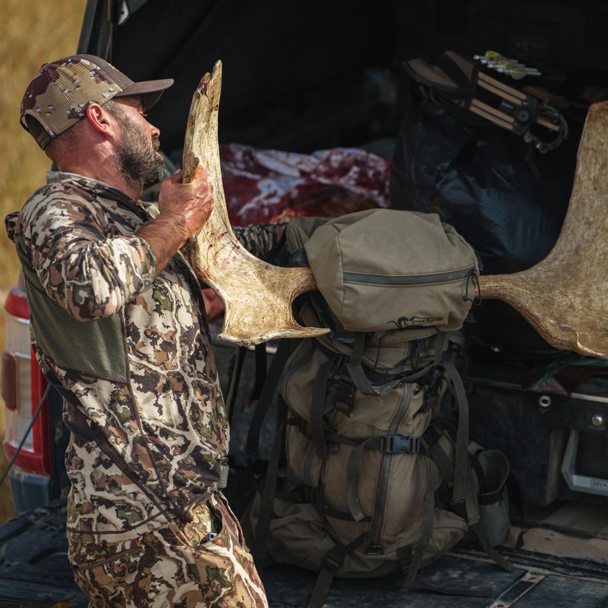 Olive green Stone Glacier backpack in truck, with man holding large light brown moose antler.